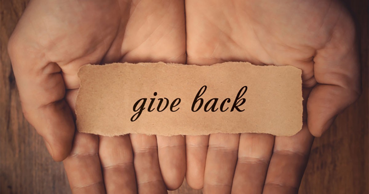 Cupped hands holding a piece of paper with "give back" written on it.