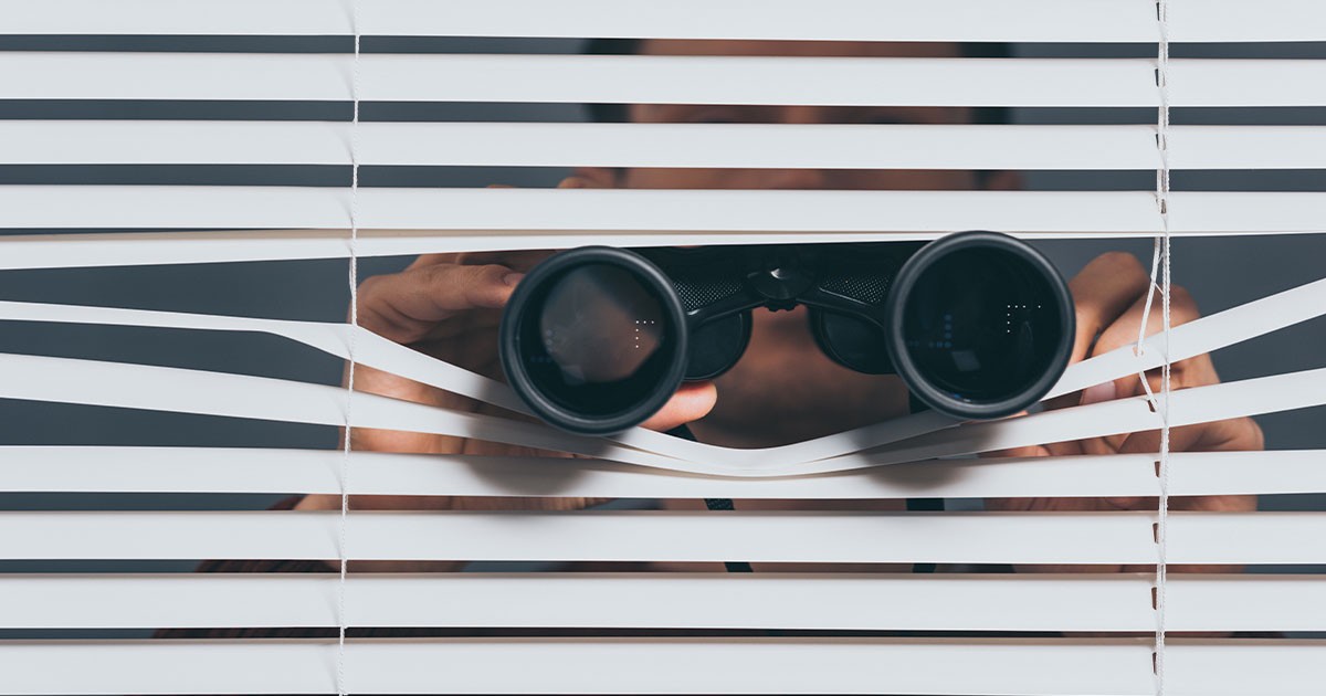 Person looking through window blinds with binoculars.