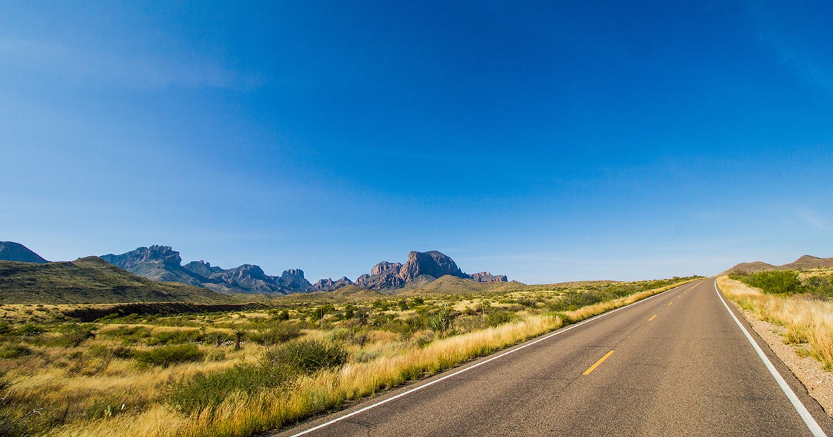 A road runs through Big Bend National Park, West Texas, and passes Chisos mountains before disappearing in to the wide open blue sky