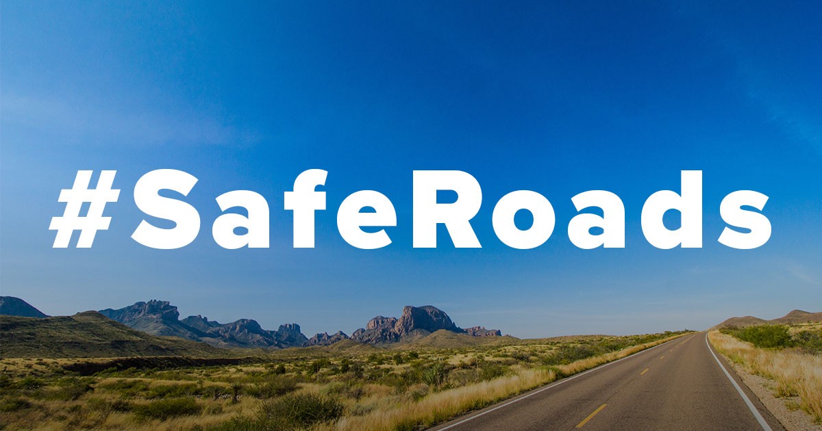 Desert road under a blue sky with #SafeRoads text