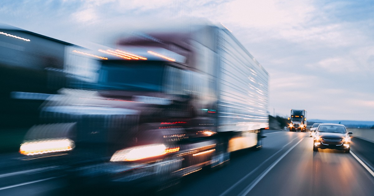 Blurred image of a semi-truck and a car driving on a highway at speed.